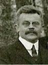 Black and white photograph of a man. It shows his head and shoulders, he is wearing a jacket and tie, and has a moustache. Style is perhaps early 20th century.